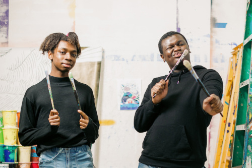 Two young men in an art studio holding paint brushes.