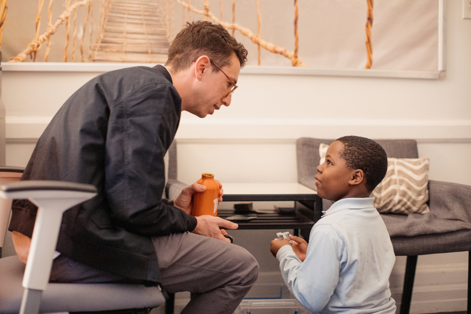 An white man sitting in an office share leans in to speak with a young Black boy