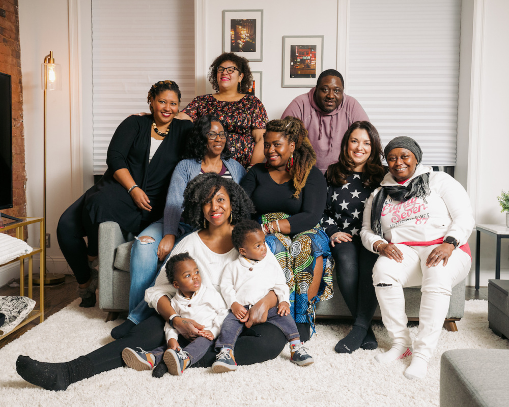 A group of Black women and children gather in a living room