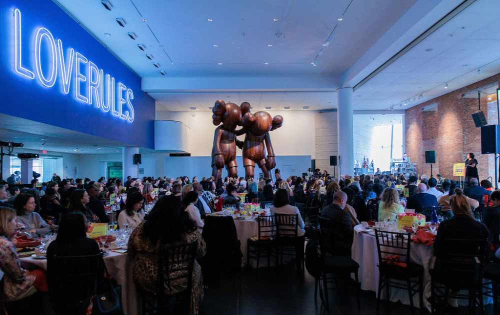 A room full of guests seated at tables in front of a large statue in the Brooklyn Museum