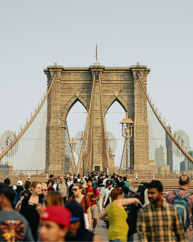 A view of the Brooklyn Bridge with a crowd of people in the foreground