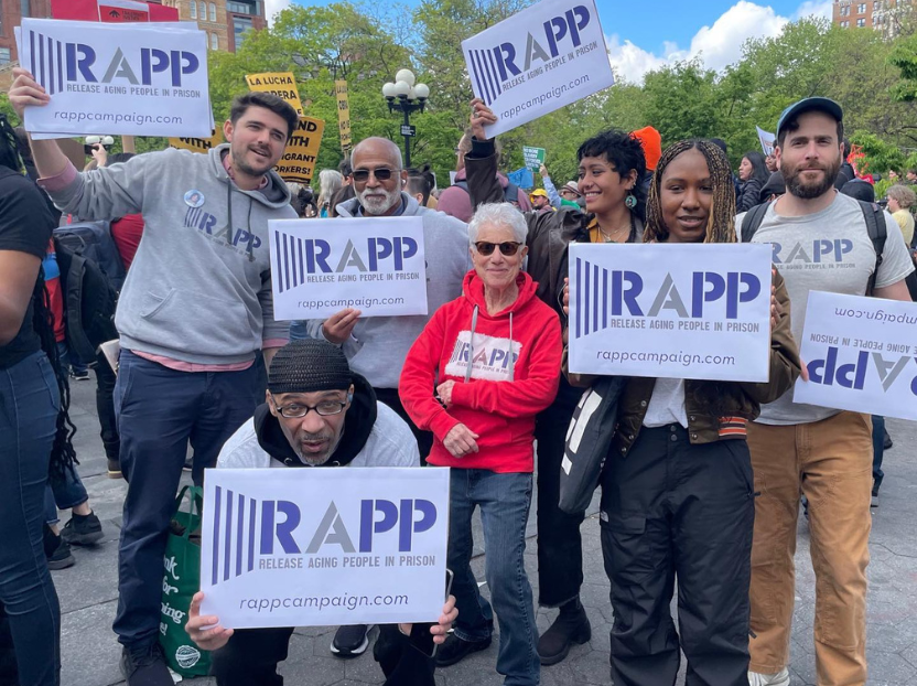 A group of people smile at the camera, holding RAPP posters.