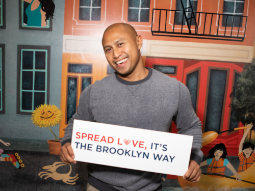 A man holding up a sign that says spread live it's the brooklyn way.