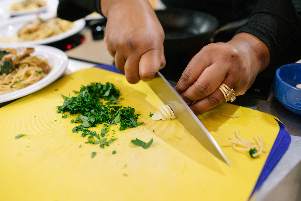 A person slicing vegetables on a yellow cutting board.