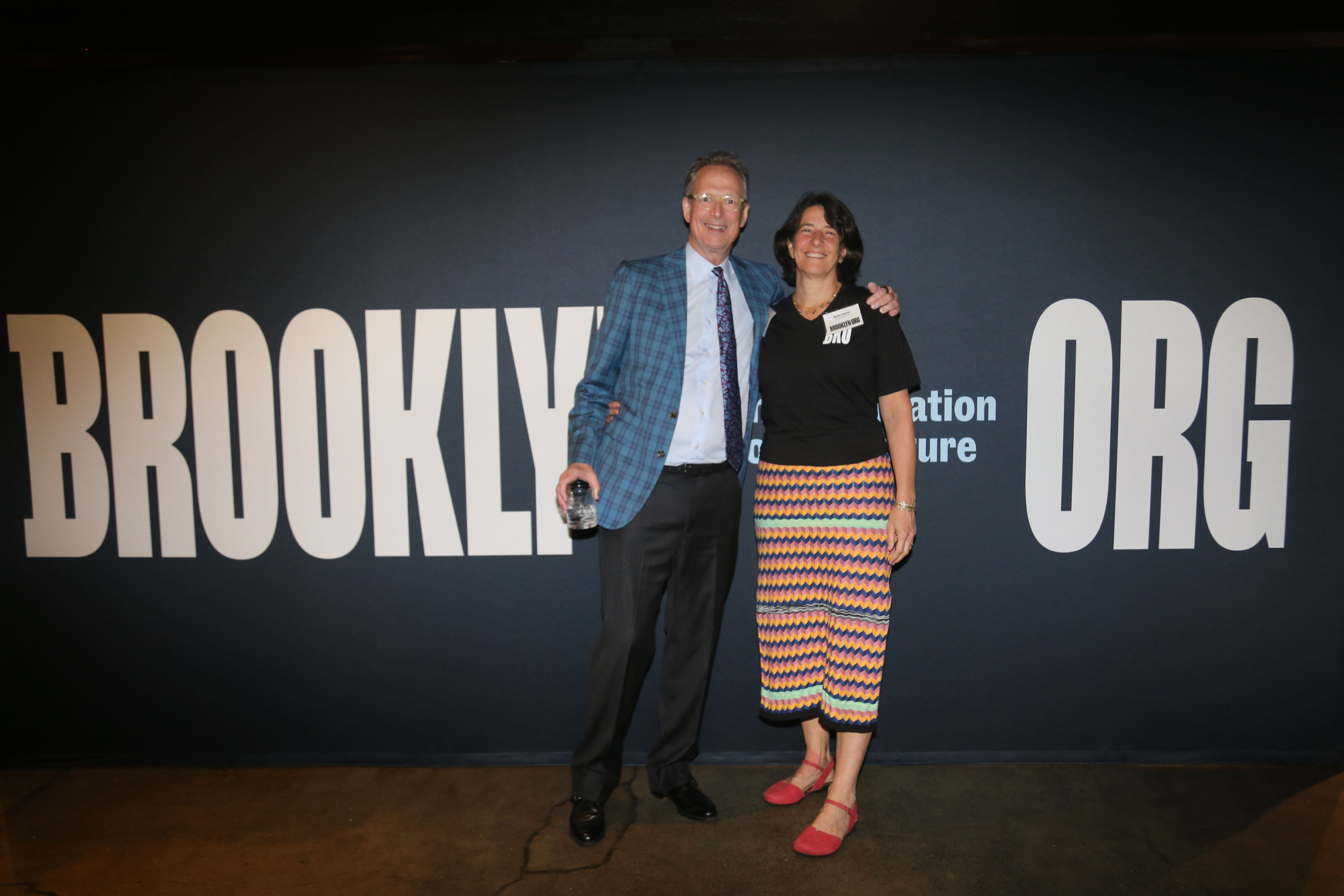 Two people standing in front of a sign that says brooklyn org.