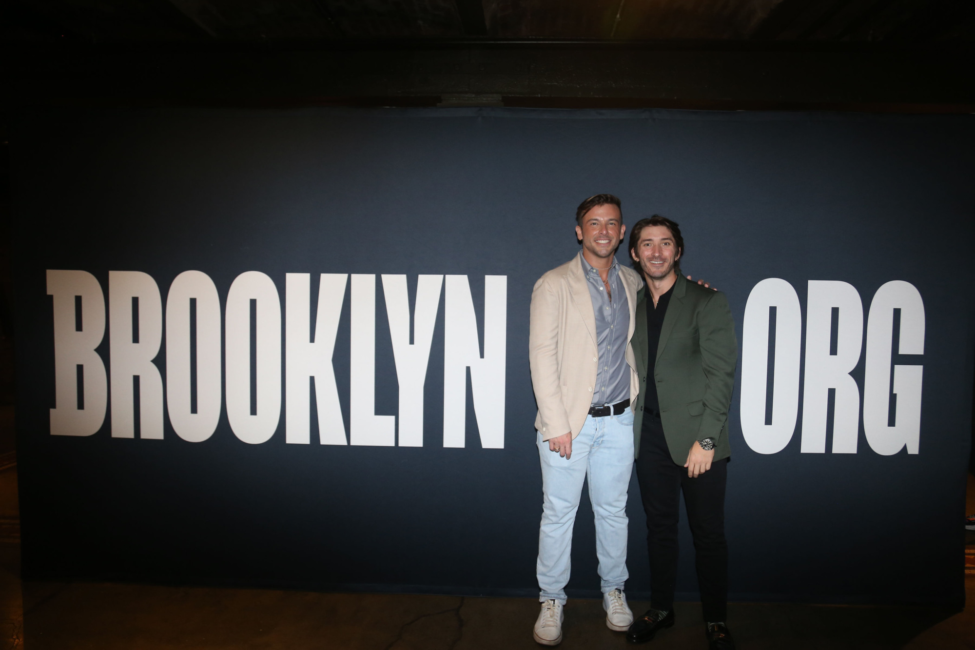 Two men standing in front of a sign that says brooklyn org.