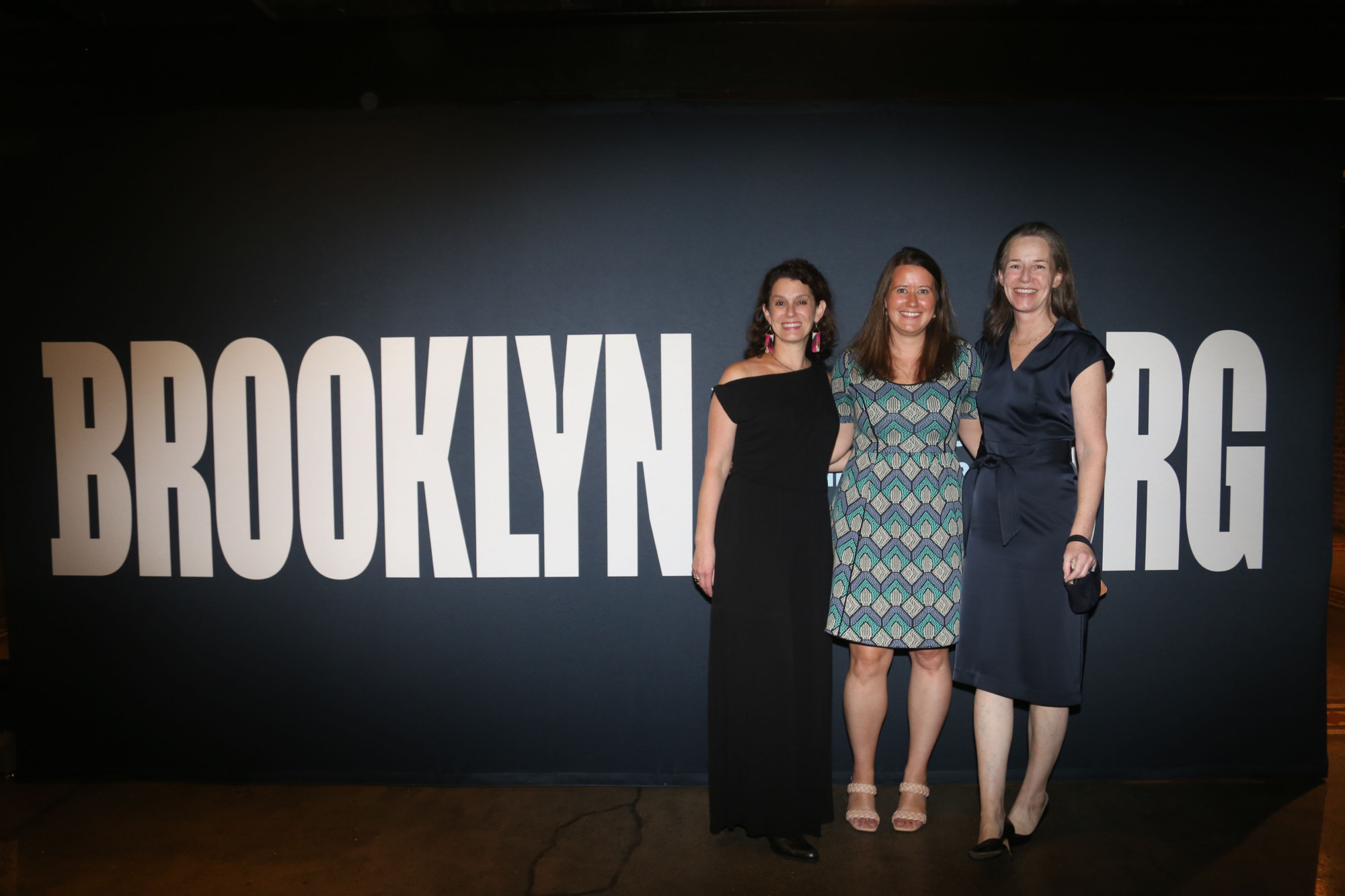 Three women standing in front of a sign that says brooklyn g.