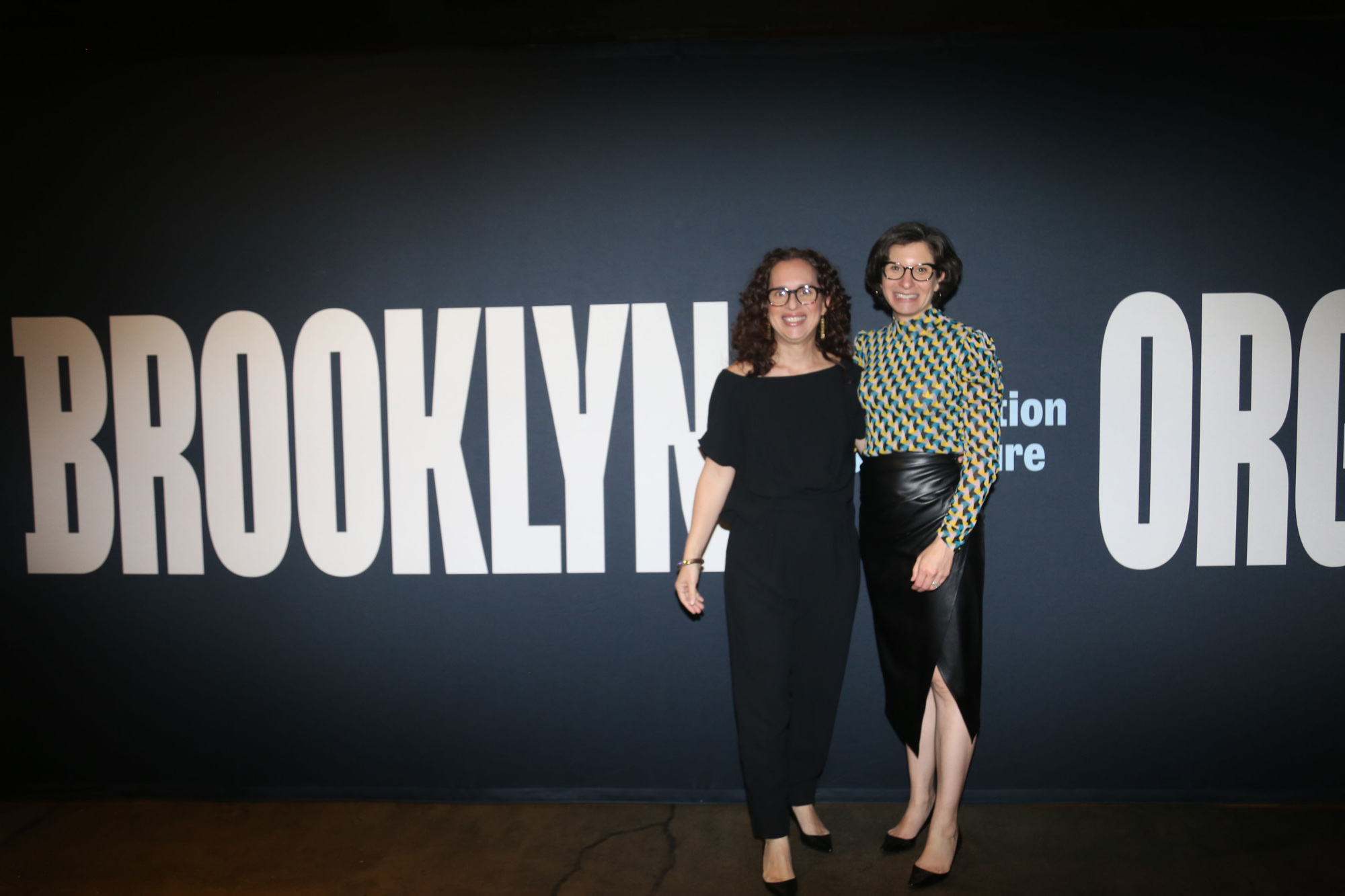 Two women standing in front of a sign that says brooklyn orchestra.