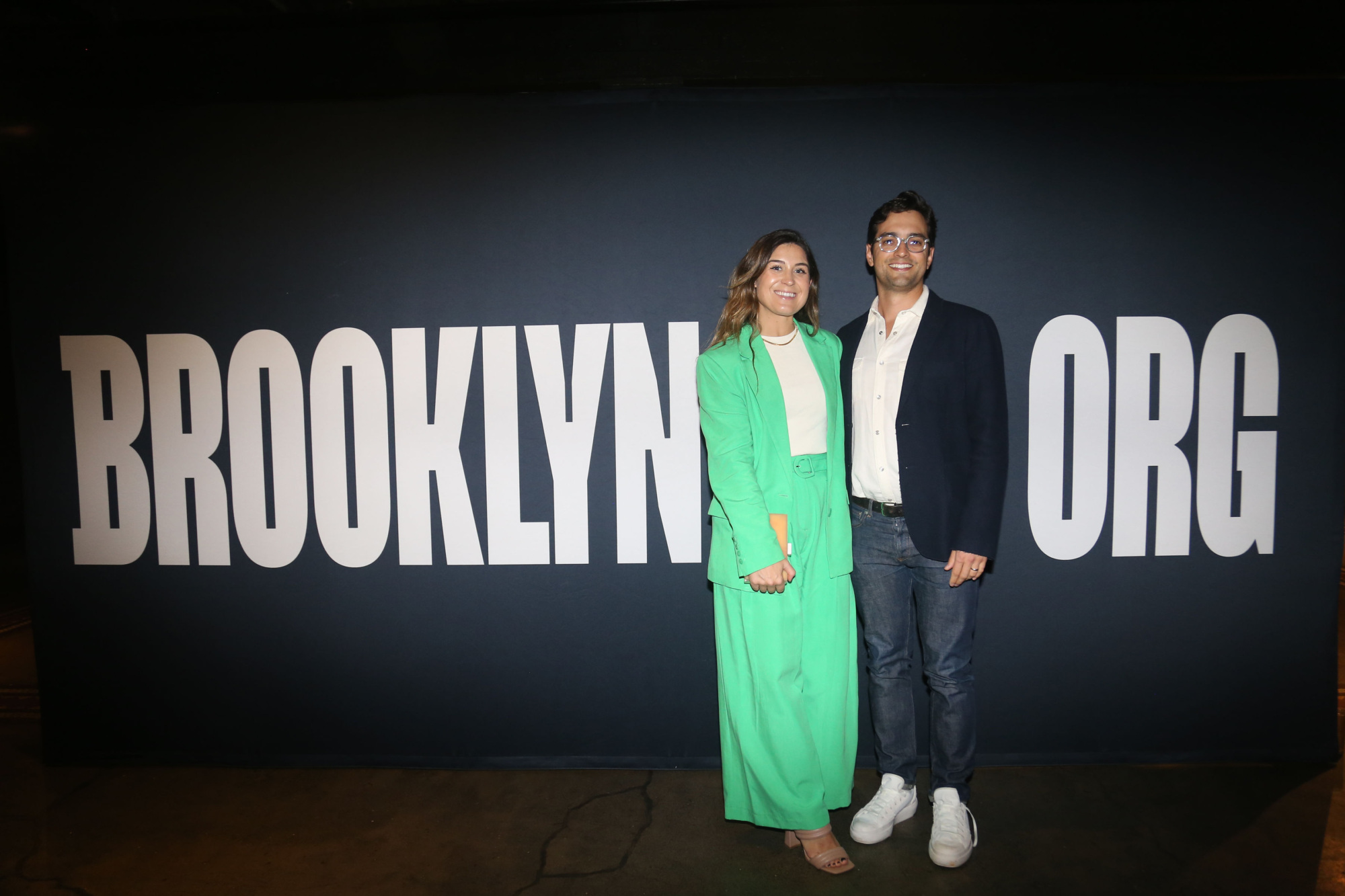 Two people standing in front of a sign that says brooklyn org.