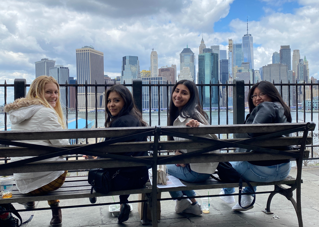 A group of girls sitting on a bench in front of a city skyline.
