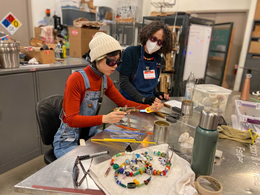 Two women working at a table in a glass studio.