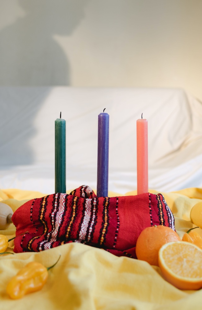 Three candles on a bed with oranges and bananas.