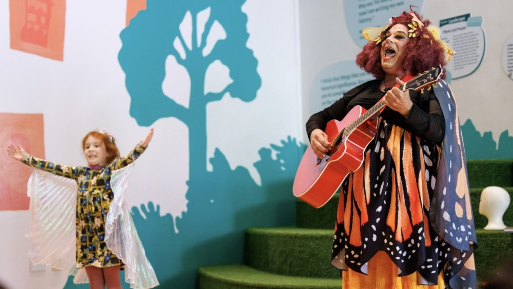 A woman dressed as a butterfly with a guitar and a little girl.