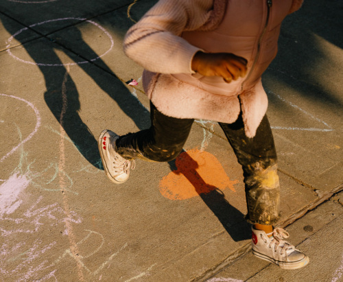 A girl is running on a sidewalk with chalk drawn on it.