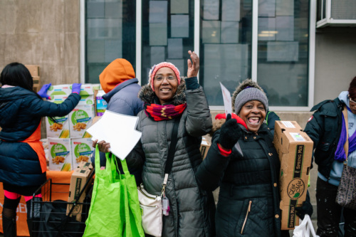 A group of people standing in front of a building with bags of food.