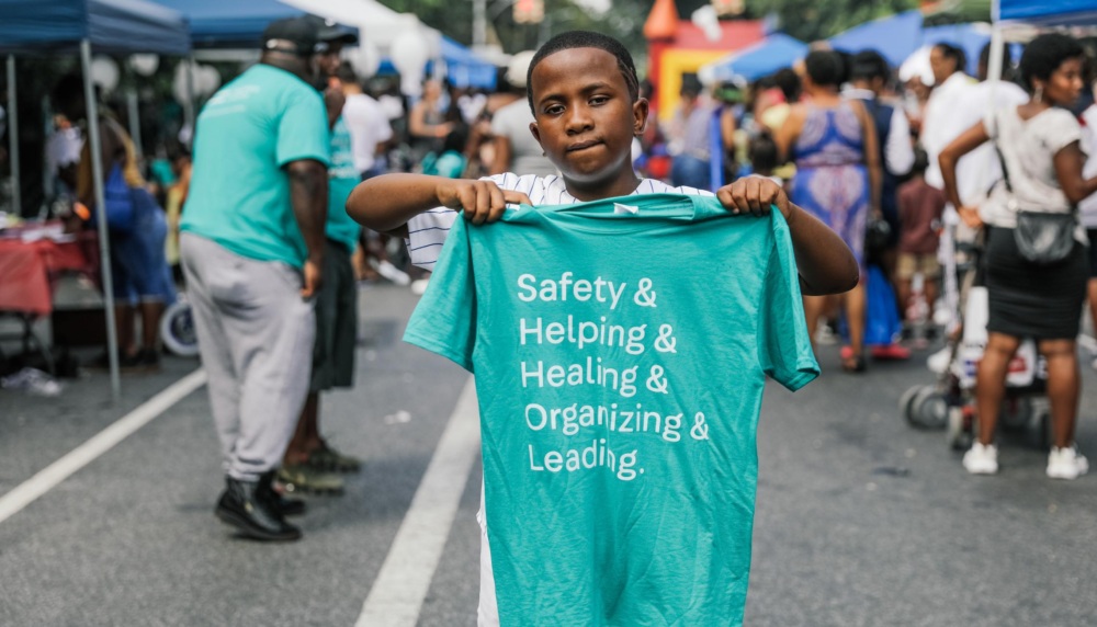 A young boy holding up a t - shirt that says safety and helping.