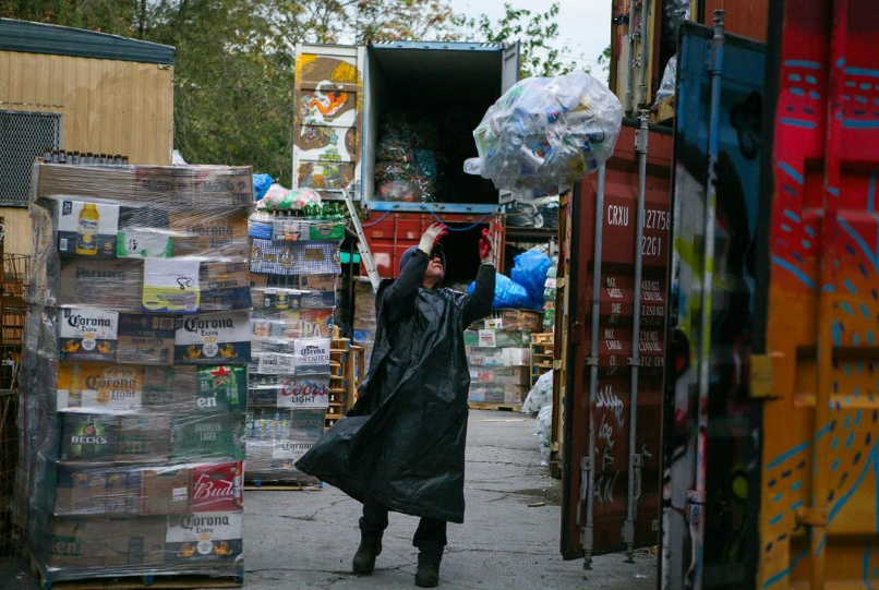 A man in a raincoat carrying a bag of trash.