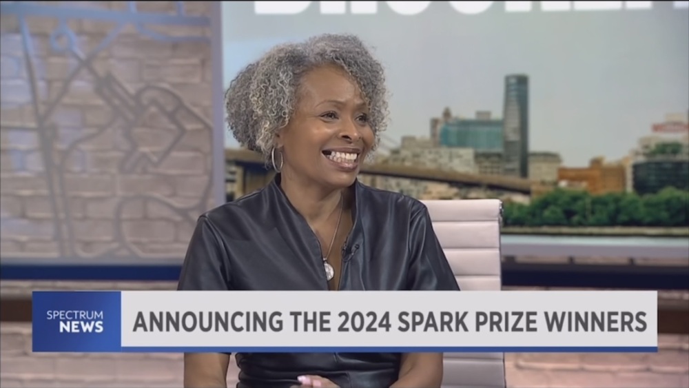 Screengrab of a news segment from NY1 Spectrum News. A Black woman smiling. The banner at the bottom says announcing the 2024 spark prize winners.