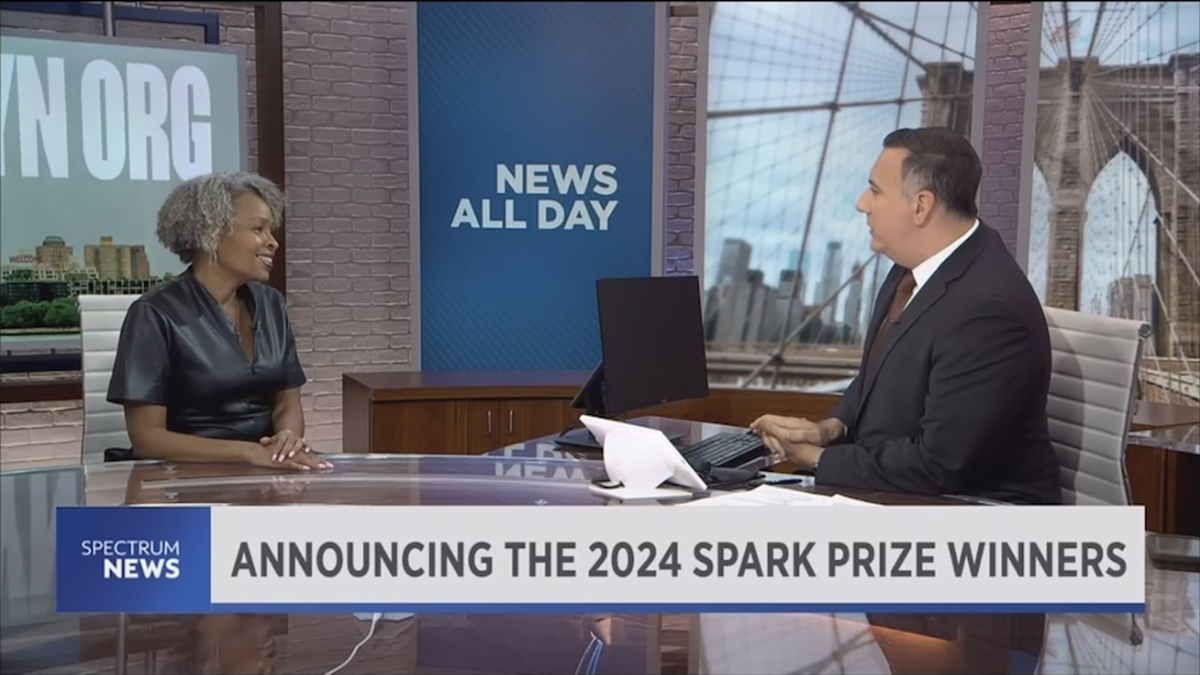 Screengrab of a news segment from NY1 Spectrum News. A Black woman sits at a table in conversation with a white reporter. The banner at the bottom says announcing the 2024 spark prize winners.