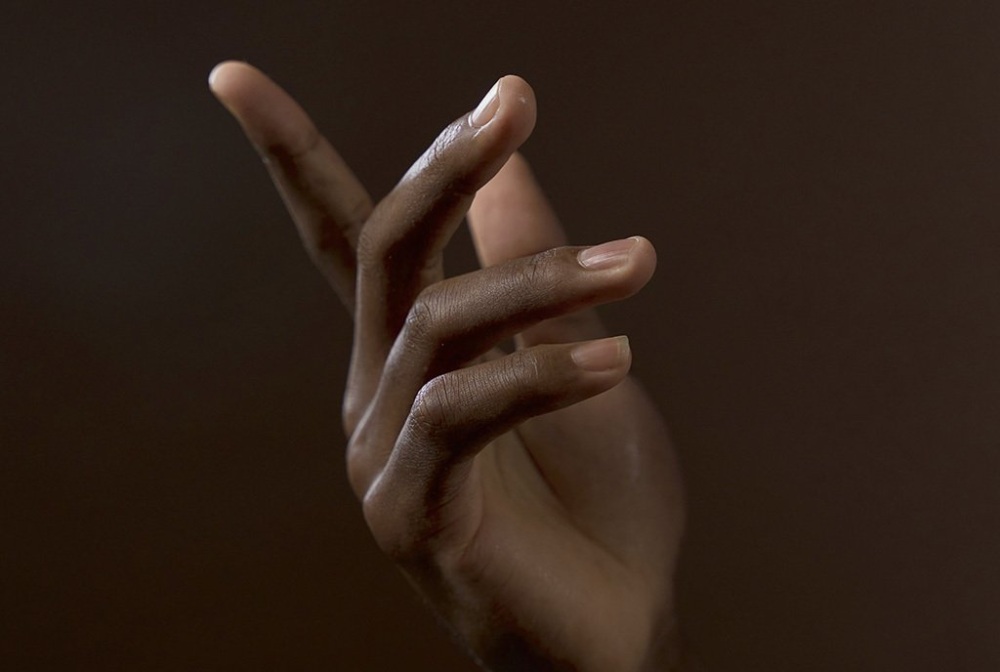 A black woman's hand showing the peace sign on a dark background.
