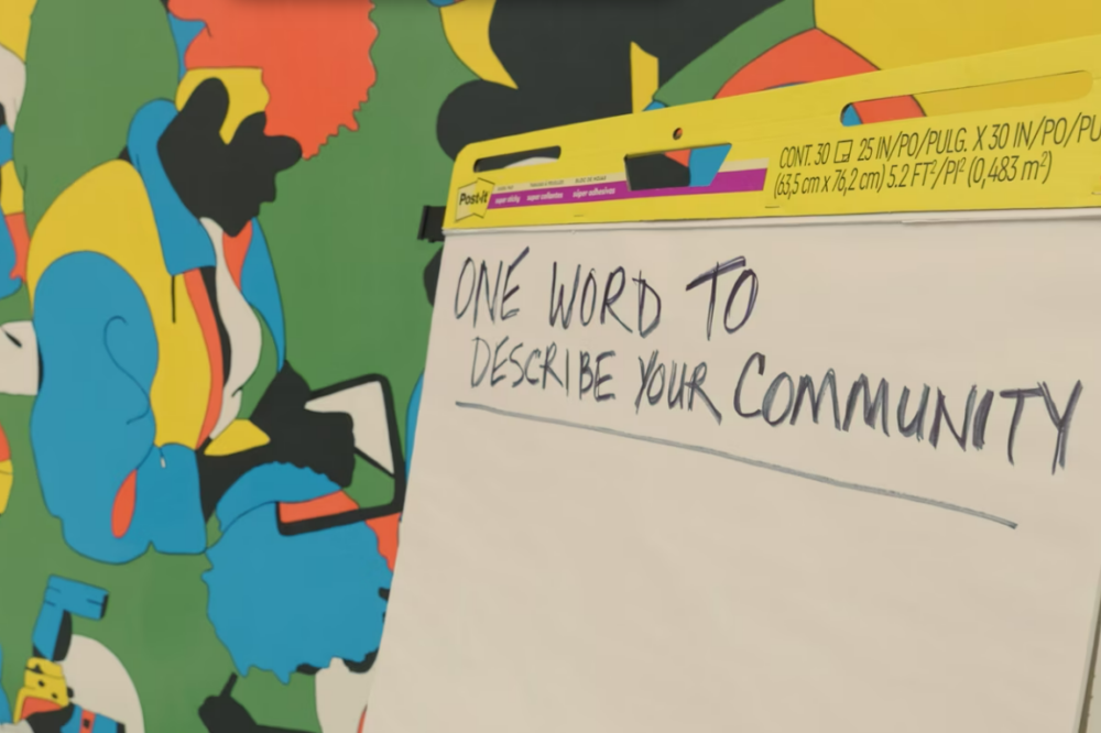 A flip chart with handwritten text "one word to describe your community" against a colorful background with abstract designs.