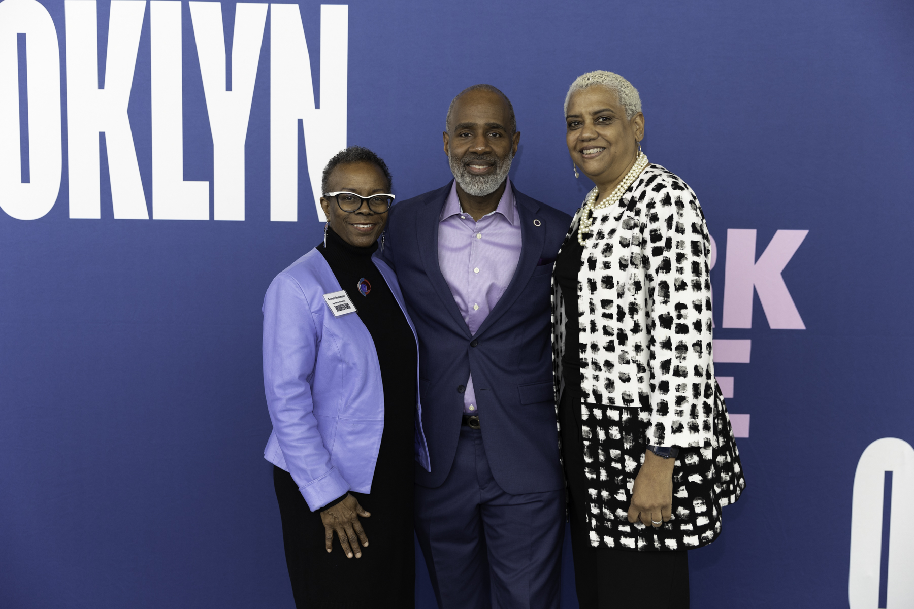 Three individuals posing for a photo at an event with a backdrop that reads "brooklyn.