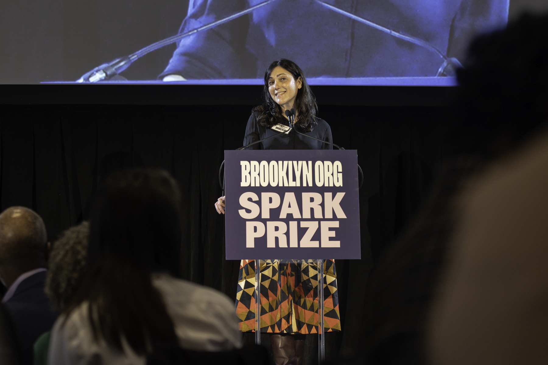 Woman speaking at a podium with the brooklyn.org spark prize sign.