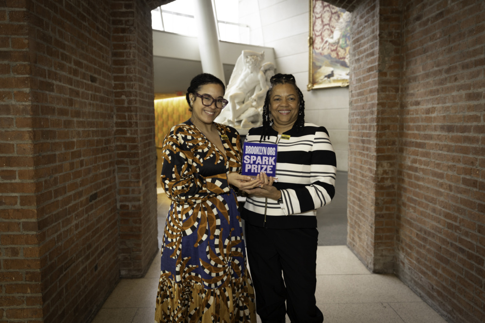 Two women smiling and holding an award together indoors.