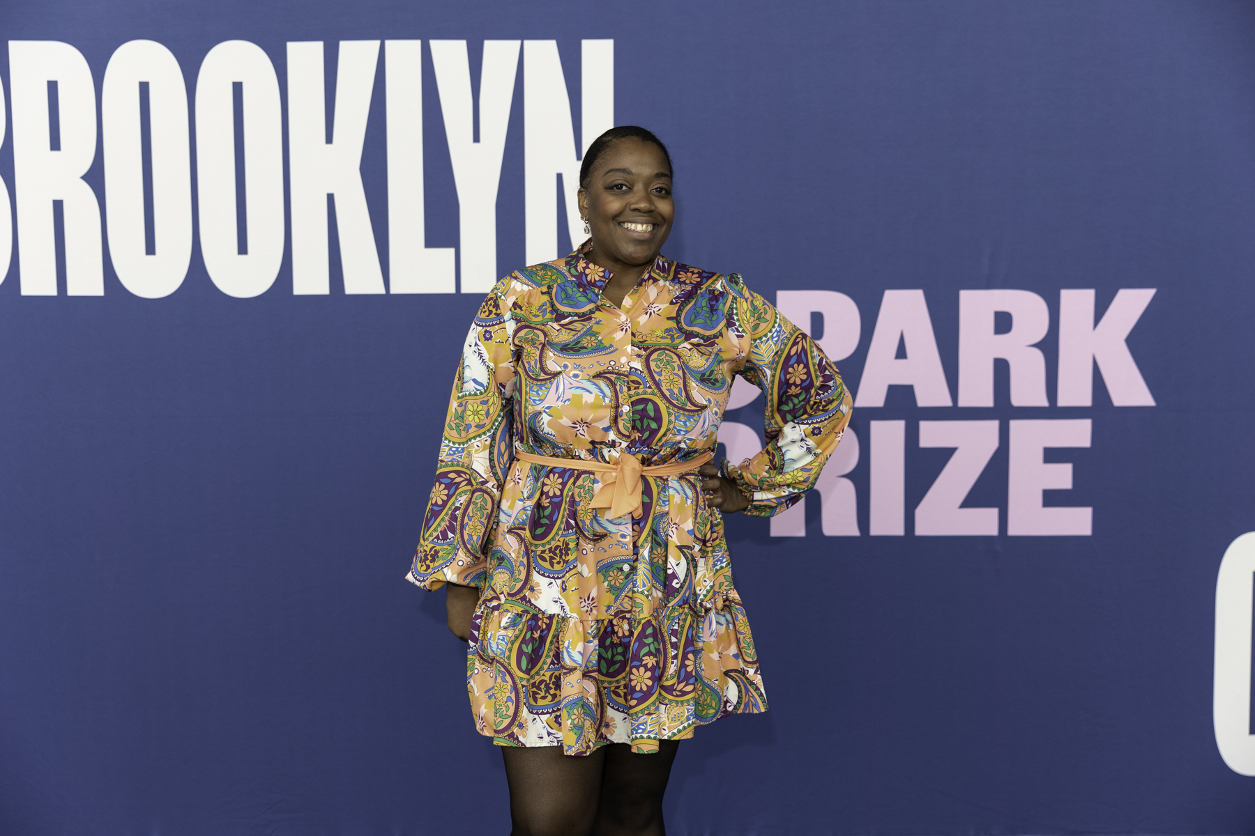 Woman in a patterned dress standing against a backdrop with the text "brooklyn park prize.