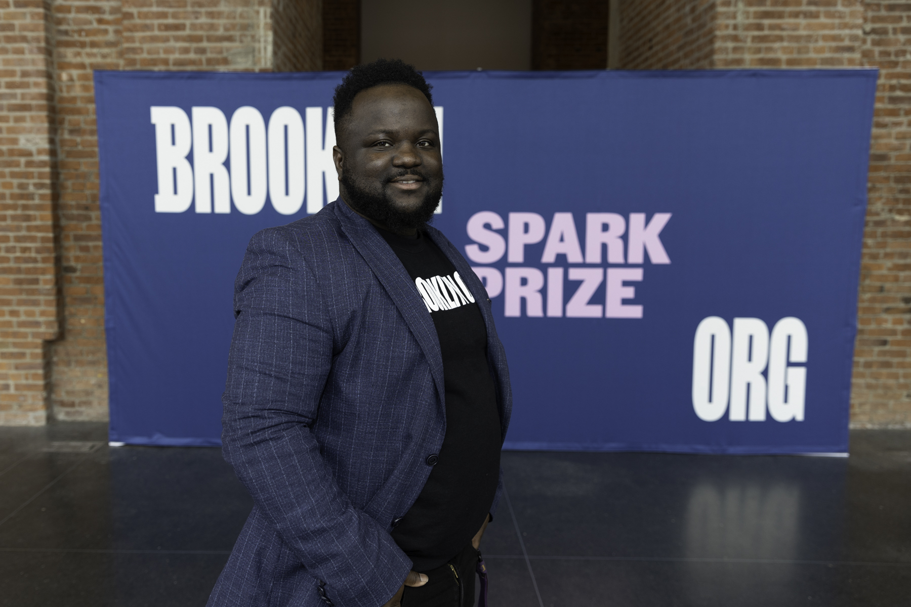 Man smiling in front of a banner reading "brooklyn spark prize.org.