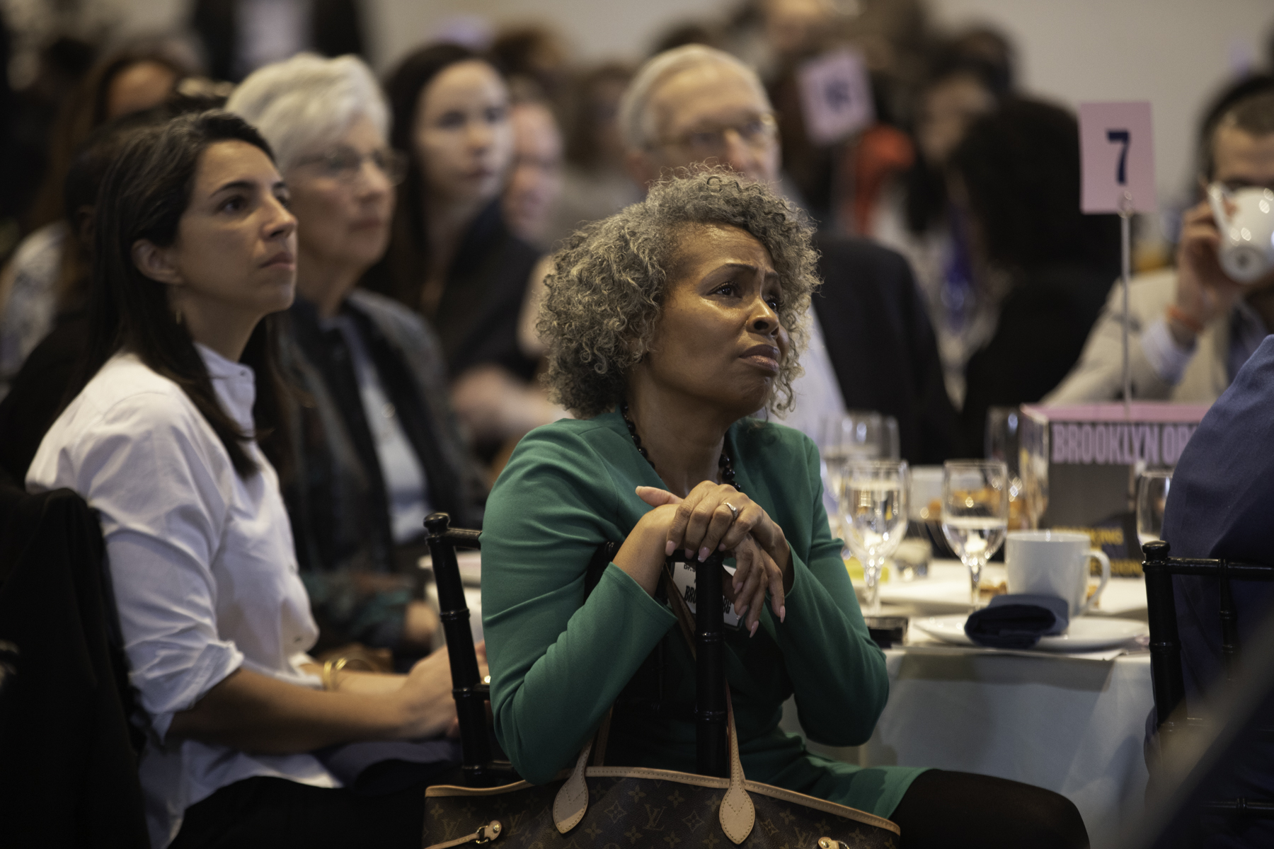 A group of attentive women sitting at a conference event, focusing on a speaker or presentation out of frame.