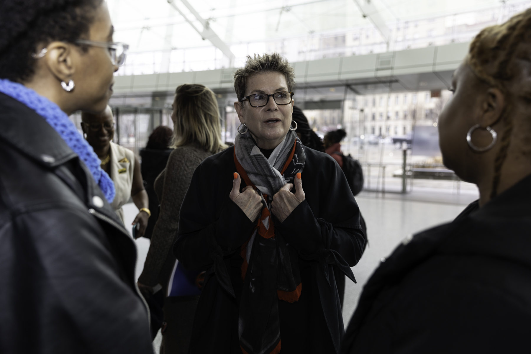 A woman gesturing during a conversation with two others in an indoor public space.