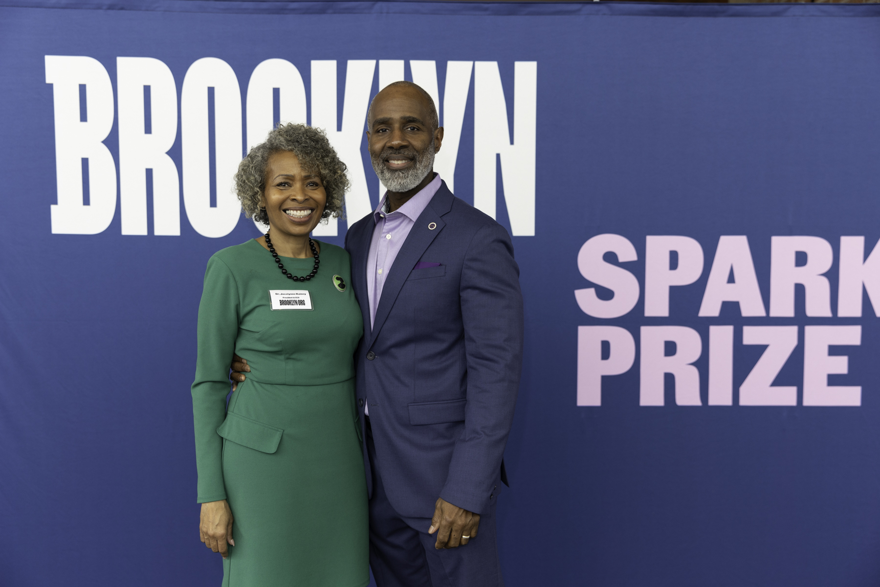 Two individuals smiling for a photo in front of a banner that reads "brooklyn spark prize.