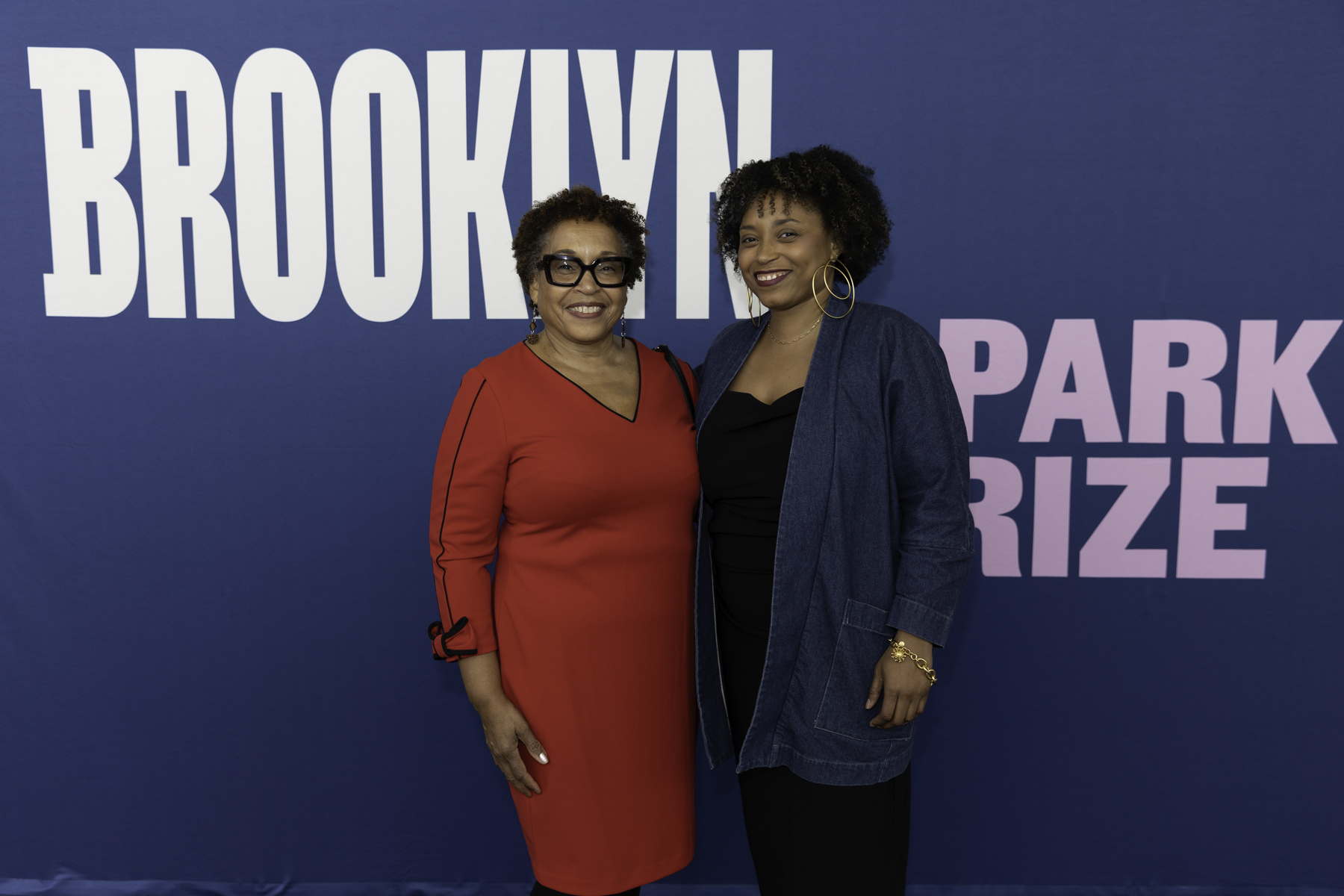 Two women posing together in front of a backdrop with the text "brooklyn park prize.
