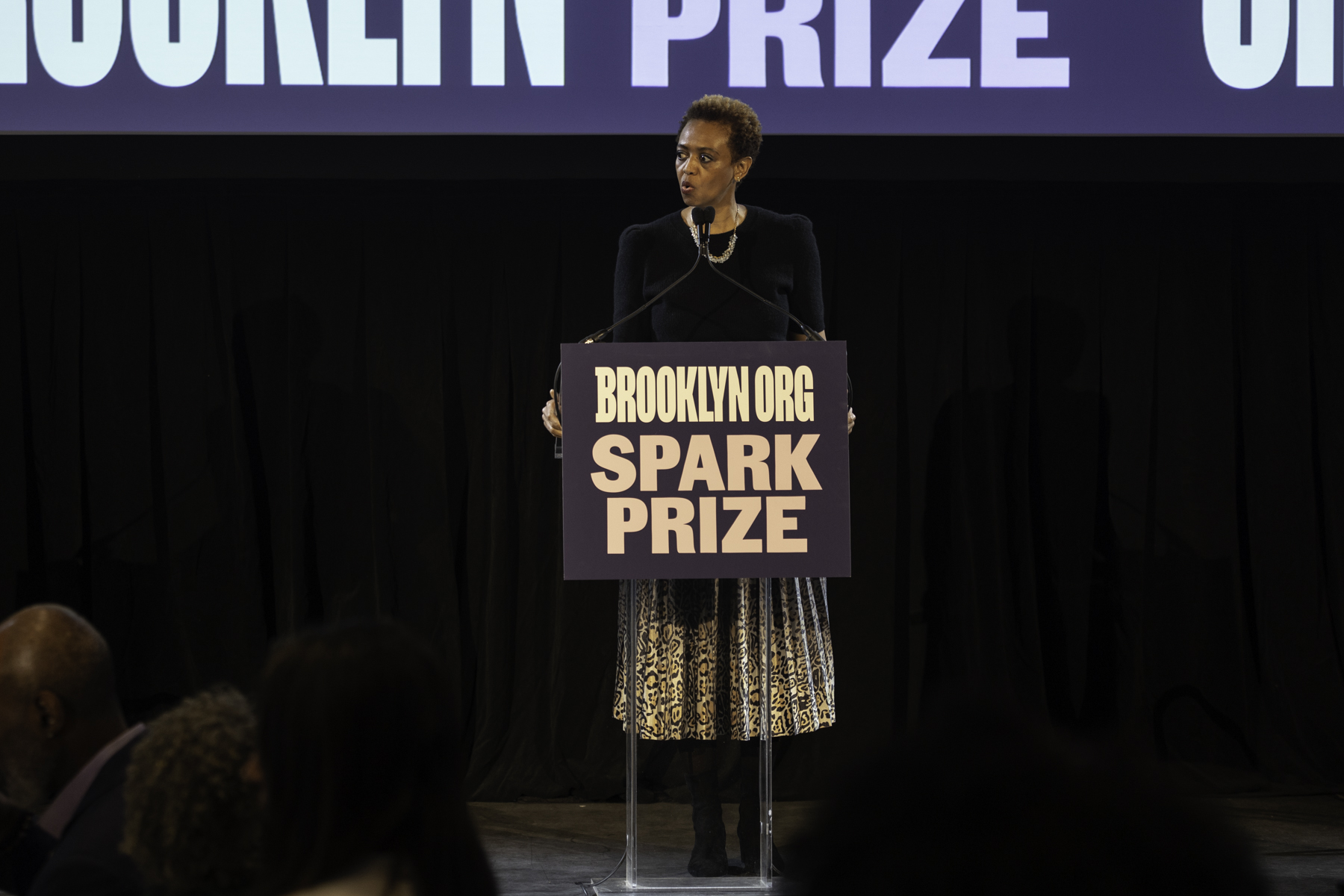 Woman speaking at a podium with the brooklyn spark prize logo.
