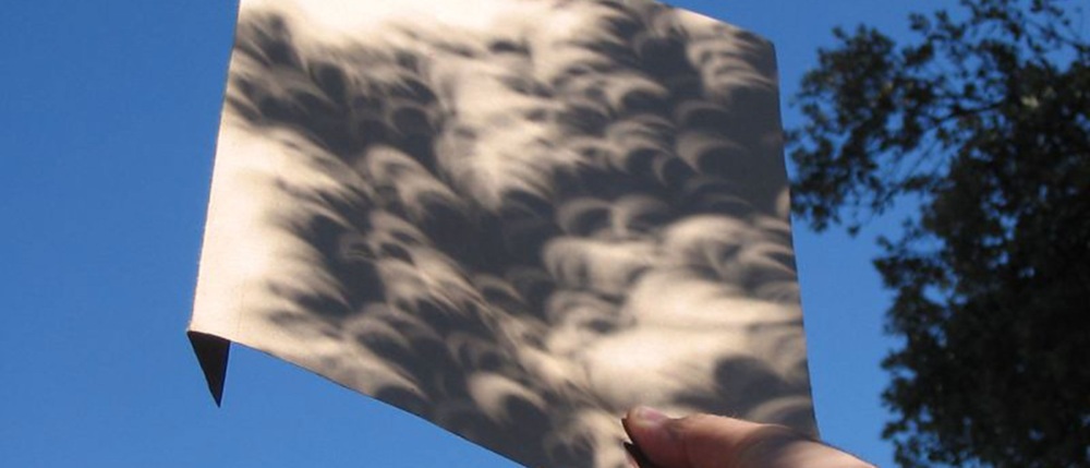 Crescent-shaped shadows cast on a piece of paper during a solar eclipse.