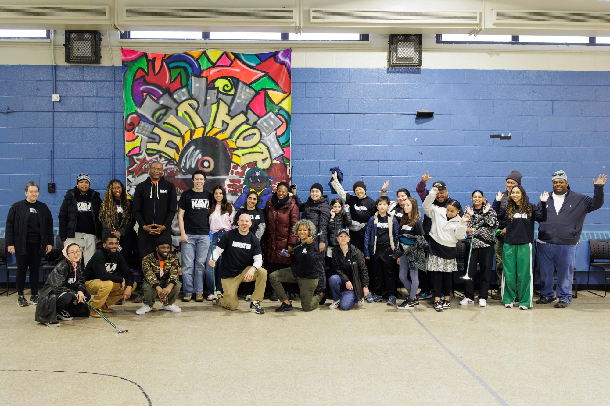 Group of diverse people posing happily in front of a colorful graffiti-style backdrop in a community center.