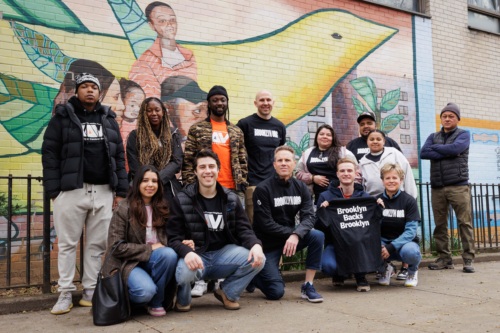 A diverse group of people posing in front of a colorful mural featuring a bird and human figures.