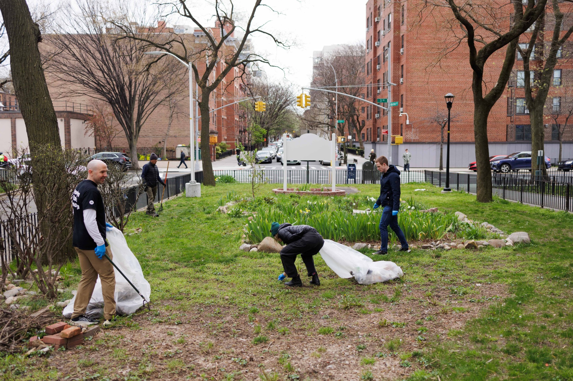 Three people participating in a community cleanup in a city park, collecting trash into large white bags.