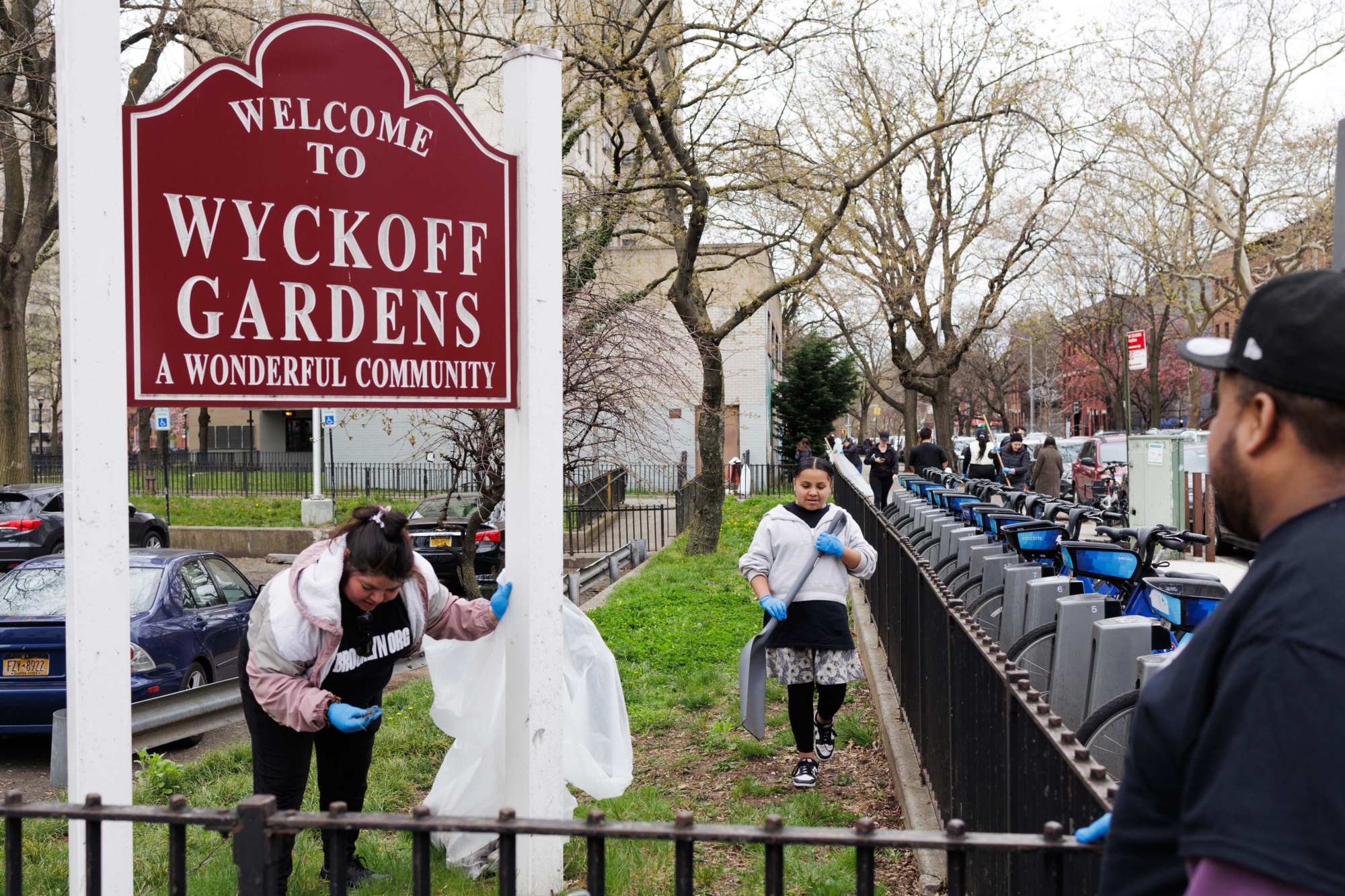 People participate in a community cleanup event at wyckoff gardens under a sign welcoming to "a wonderful community.