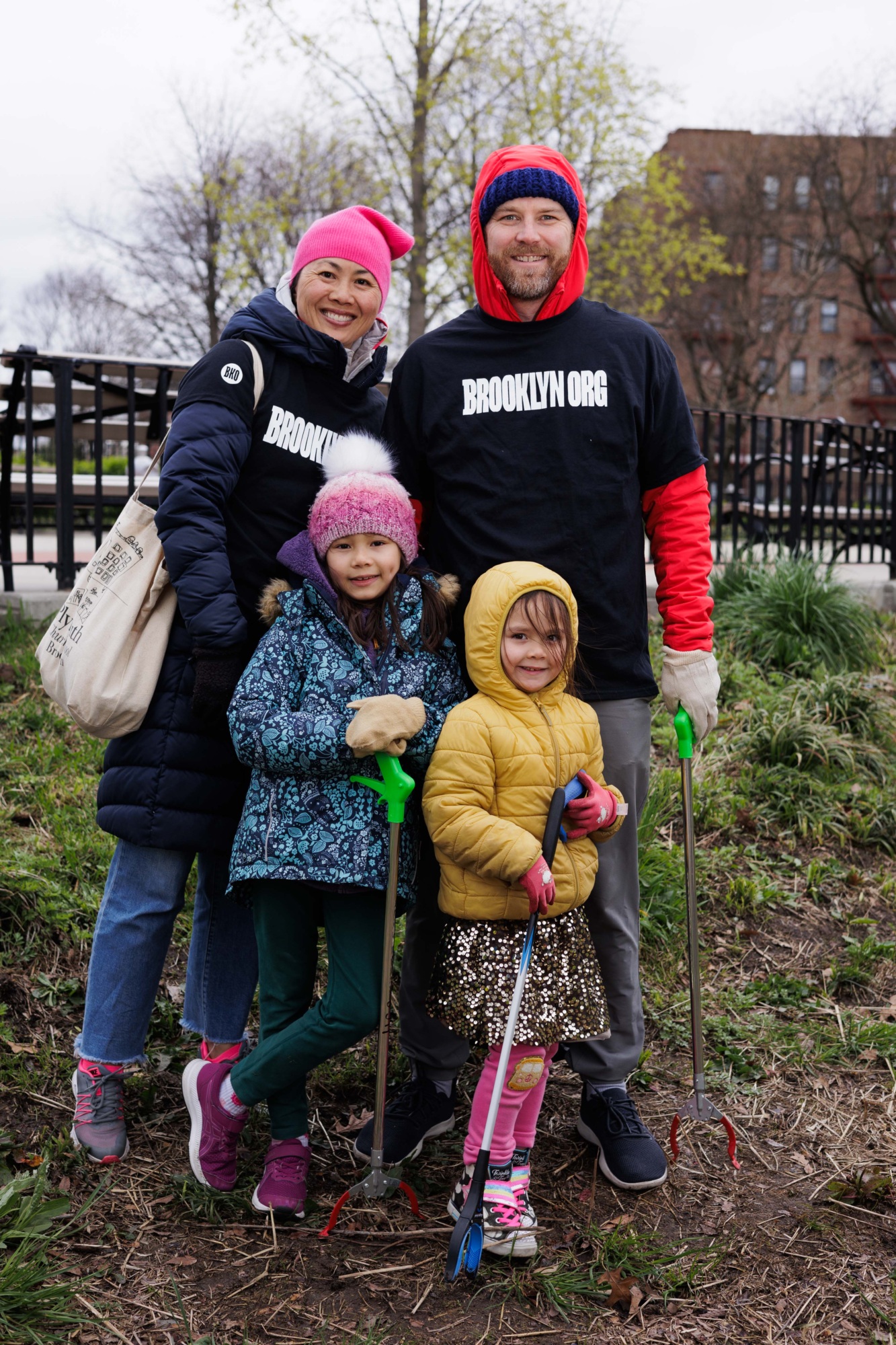Family of four with gardening tools posing outside, wearing winter hats and smiling at the camera.