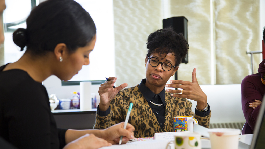 A Black woman gestures while speaking during a meeting.