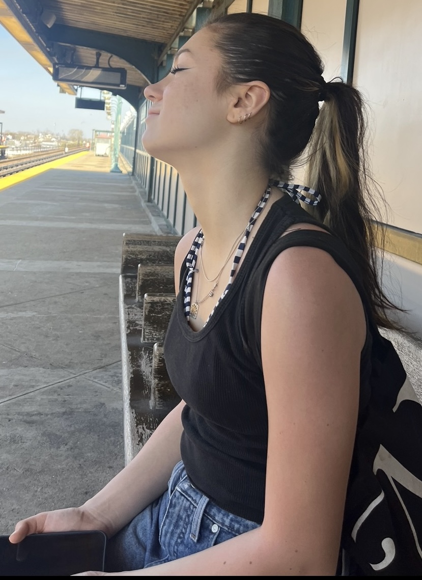 Young woman smiling and looking upwards while sitting at a train station platform.