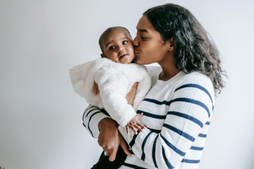 A Black woman affectionately kissing a baby she's holding in her arms.