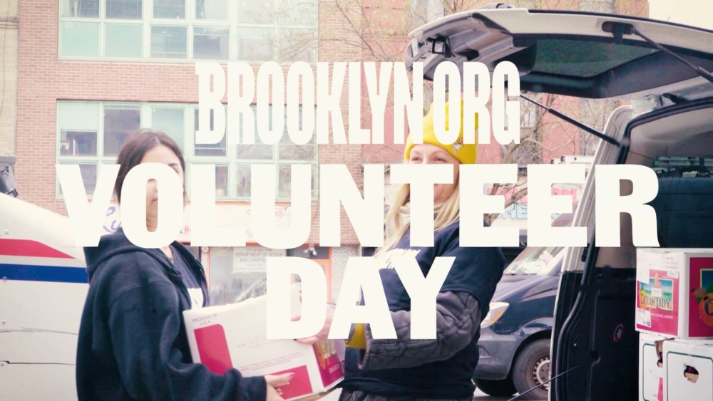 Two people standing by an open car trunk handing out books with a "brooklyn volunteer day" text overlay.