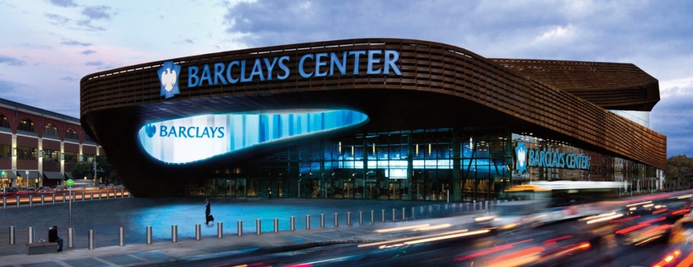 Panoramic view of Barclays Center at dusk with bustling street traffic and illuminated signage.