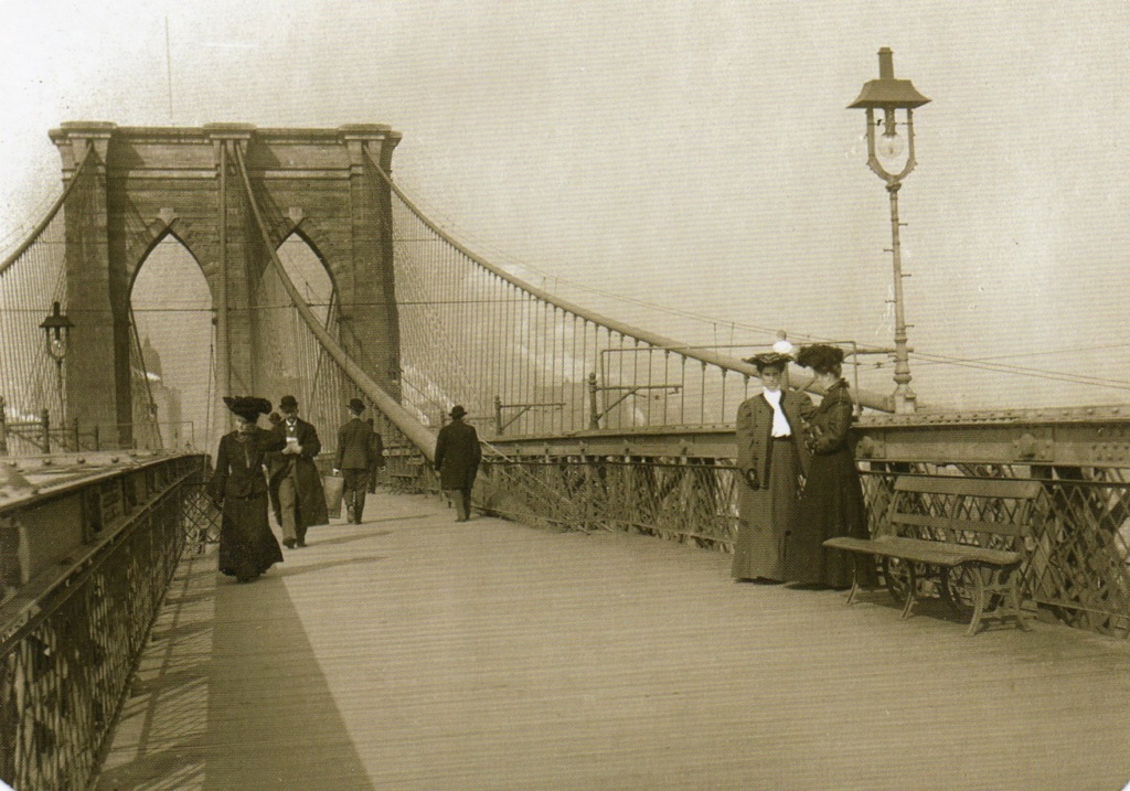 A sepia-toned photograph showing people walking and standing on the Brooklyn Bridge, with the bridge’s cables and arches visible in the background.