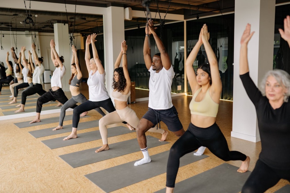 A group of people practicing yoga in a studio, performing a standing pose with arms raised.
