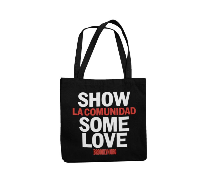 A black tote bag with the words "SHOW LA COMUNIDAD SOME LOVE" and "BROOKLYN.ORG" printed in white and red on its front.