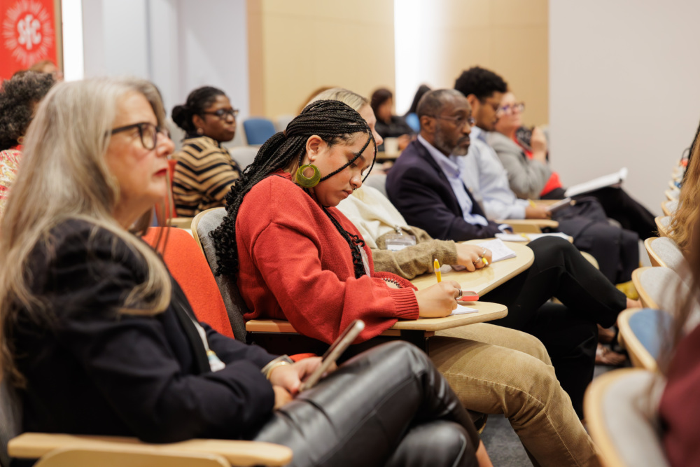 A group of people sitting in a lecture hall, taking notes and listening attentively to a presentation.